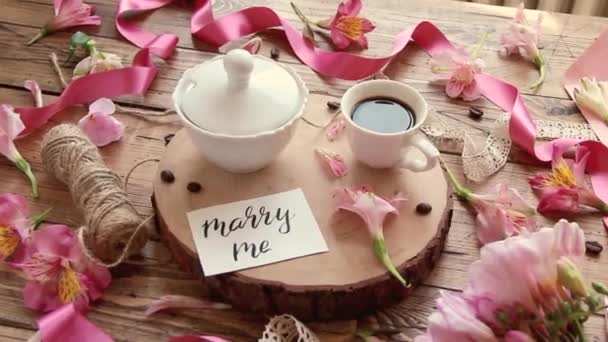 Tarjeta MARRY ME cerca de café y flores en una mesa de madera - Imágenes, Vídeo