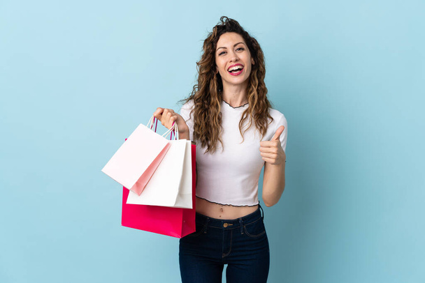 Mulher caucasiana jovem isolado no fundo azul segurando sacos de compras e com o polegar para cima - Foto, Imagem