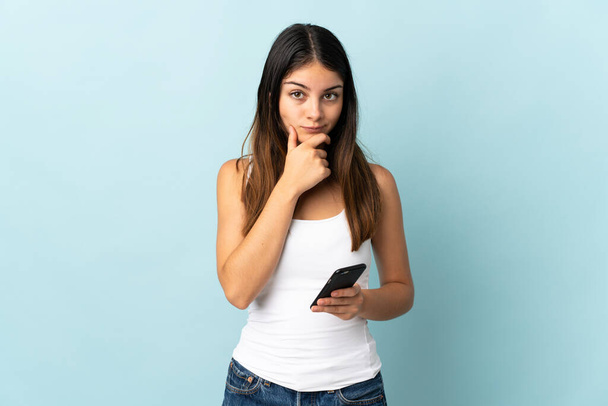 Молода біла жінка використовує мобільний телефон ізольовано на синьому фоні мислення
 - Фото, зображення