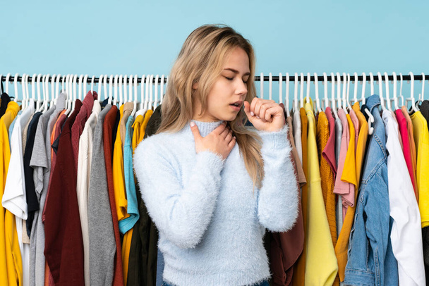 Подростковая русская девушка покупает одежду на голубом фоне страдает от кашля и плохо себя чувствует. - Фото, изображение