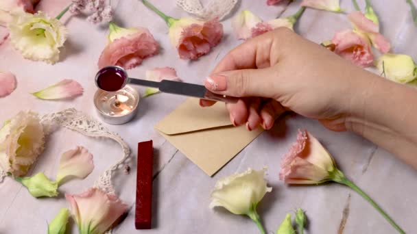 Ruce nalít roztavený vosk a těsnění na obálku blízko růžových květin na mramorovém stole zblízka  - Záběry, video