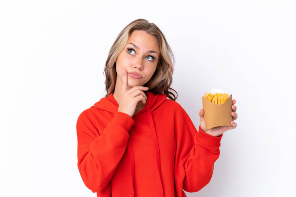 Молодая русская девушка держит жареные чипсы на белом фоне, испытывая сомнения, глядя вверх - Фото, изображение