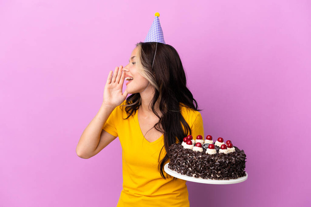 Adolescente chica rusa sosteniendo pastel de cumpleaños aislado sobre fondo púrpura gritando con la boca abierta hacia un lado - Foto, imagen