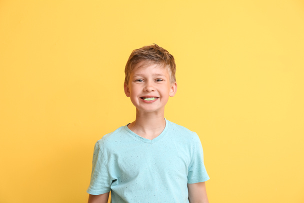 Little boy in blue t-shirt chewing gum on yellow background - Фото, изображение