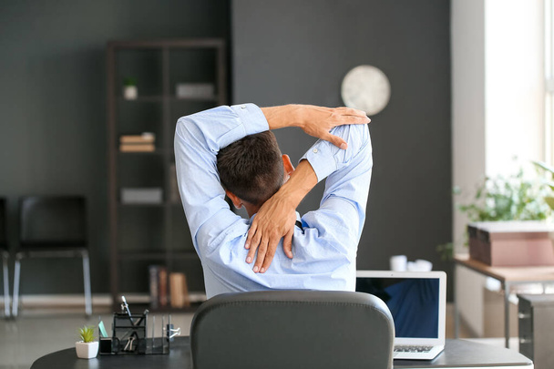 Joven hombre de negocios estirando su columna vertebral mientras trabaja en la oficina - Foto, Imagen