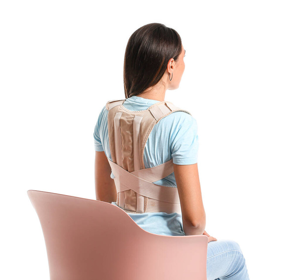 Young woman in back brace sitting on chair against white background - Фото, изображение