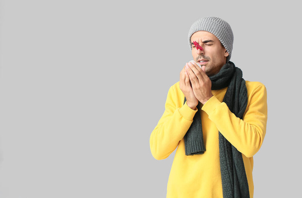 Nemocný mladý muž s špendlíkem na nose na šedém pozadí - Fotografie, Obrázek