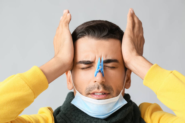 Jeune homme malade avec une pince à linge sur le nez sur fond gris - Photo, image