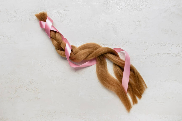 Geflochtenes rotes Haar zur Spende mit rosa Schleife auf hellem Hintergrund - Foto, Bild