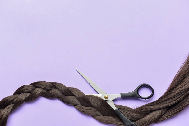 Braided brunette hair for donation with scissors on lilac background - 写真・画像