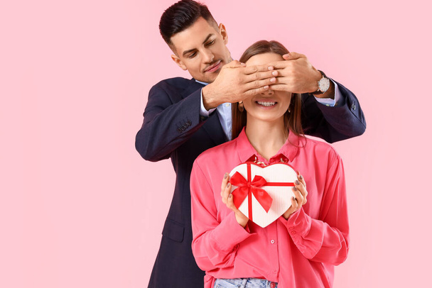 Happy young couple with gift on pink background. Valentine's Day celebration - Zdjęcie, obraz