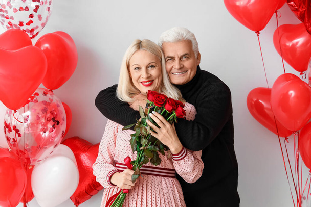 Ευτυχισμένο ώριμο ζευγάρι με λουλούδια και μπαλόνια στο φως φόντο. Γιορτή του Αγίου Βαλεντίνου - Φωτογραφία, εικόνα