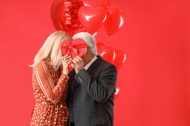 Happy mature couple with gift and balloons on color background. Valentine's Day celebration - Foto, Imagem