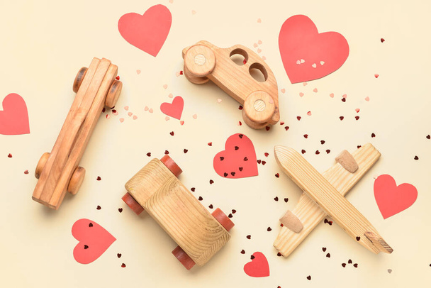 Auto in legno, aeroplano, cuori di carta e coriandoli su sfondo beige. Festa di San Valentino - Foto, immagini