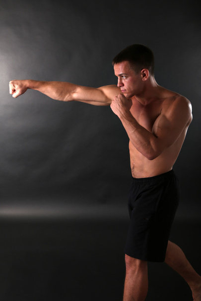 Handsome young muscular sportsman boxing on dark background - Foto, Bild