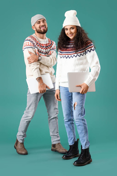 暖かいセーターを着た幸せな若いカップル,色の背景にタブレットやラップトップと, - 写真・画像