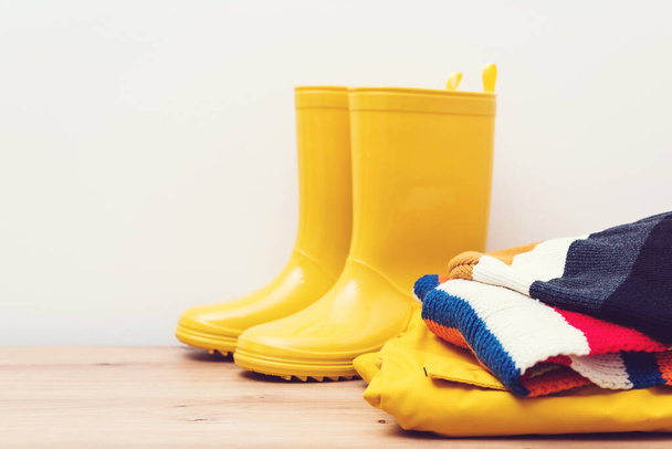 Κίτρινες μπότες βροχής και στολή outsummer. Φθινοπωρινή μόδα Κομψές μπότες και παλτό σε ξύλινο ράφι. Ρούχα και μπότες. Εποχιακά καταστήματα και πωλήσεις. - Φωτογραφία, εικόνα
