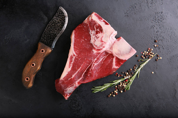 Raw meat. Steak marble beef, t-bone on a dark black board with spices, rosemary, iron knife on a black table. Background image, copy space, flatlay, top view - Φωτογραφία, εικόνα