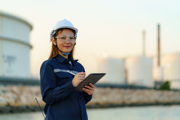 Asian engineer woman are checking the maintenance of the oil refinery factory at evening via digital tablets - Fotó, kép