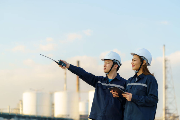 Asian engineers, man and woman are checking the maintenance of the oil refinery factory at evening via digital tablets - Photo, Image