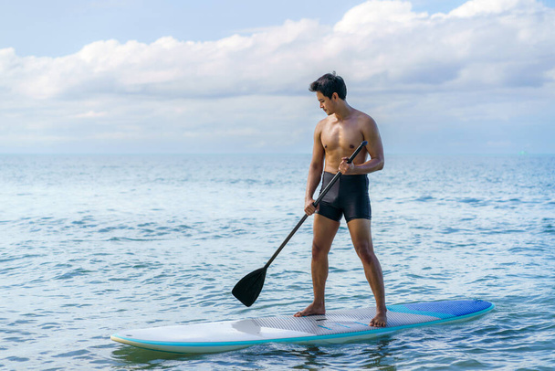Asian man exercising sup board in turquoise tropical clear waters in summer day - 写真・画像