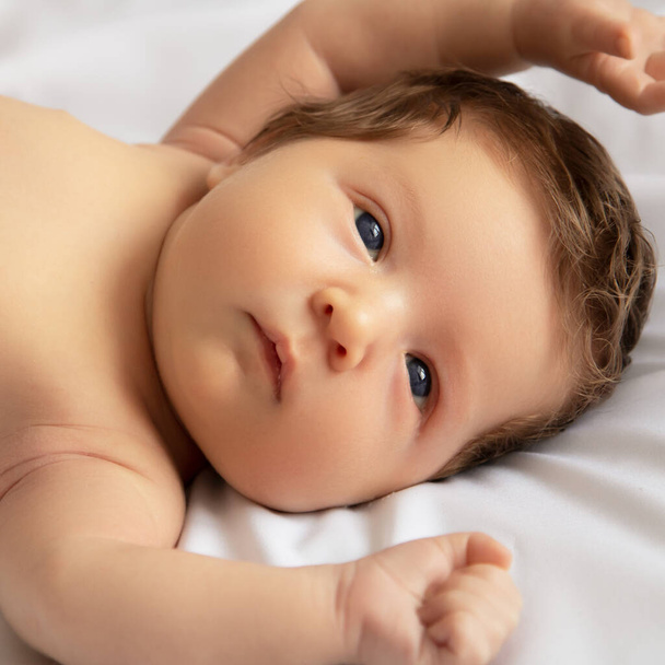 Newborn baby in a wrap on white blanket. Beautiful portrait of little child girl 7 days, one week old. Baby lying on back on white background - Φωτογραφία, εικόνα