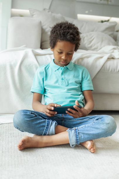 Child sitting cross-legged on the floor using mobile phone - Φωτογραφία, εικόνα