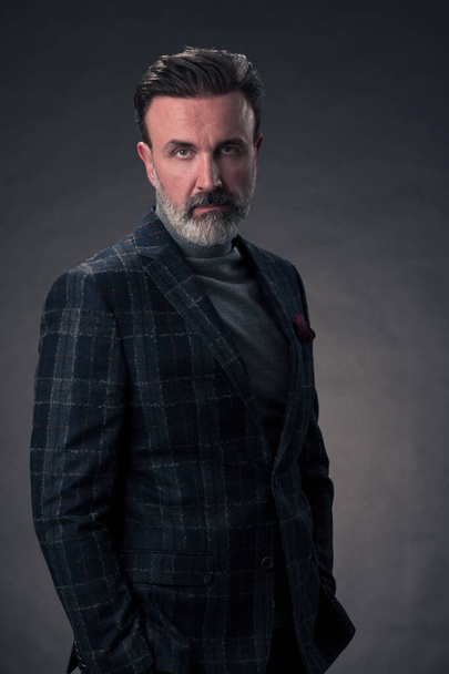 Portrait of a stylish elegant senior businessman with a beard and casual business clothes in photo studio isolated on dark background gesturing with hands. High quality photo - Fotografie, Obrázek