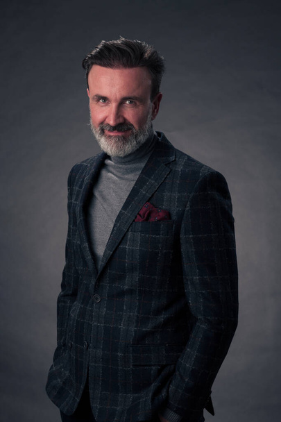 Portrait of a stylish elegant senior businessman with a beard and casual business clothes in photo studio isolated on dark background gesturing with hands. High quality photo - 写真・画像