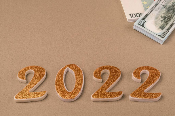 Golden numbers 2022 and bundles with money in dollars and euros on a beige background. Copy space - Foto, imagen