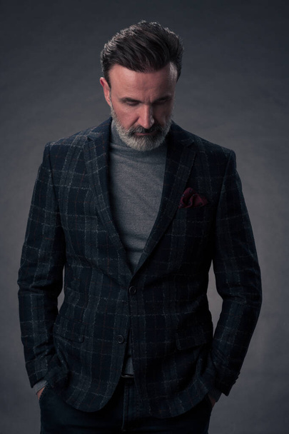 Portrait of a stylish elegant senior businessman with a beard and casual business clothes in photo studio isolated on dark background gesturing with hands. High quality photo - Foto, Bild