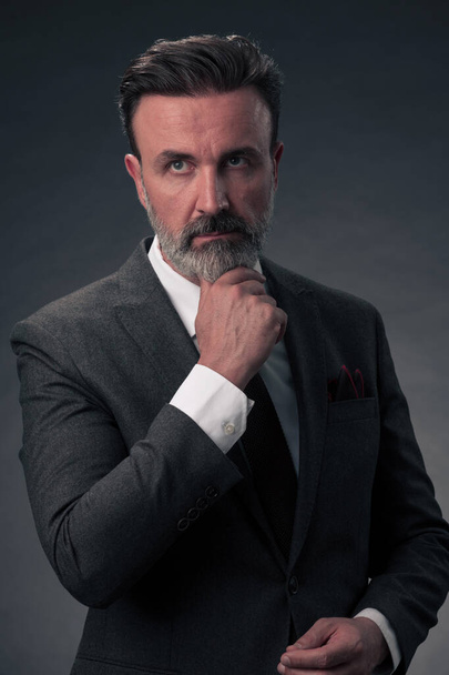 Portrait of a stylish elegant senior businessman with a beard and casual business clothes in photo studio isolated on dark background gesturing with hands. High quality photo - Photo, image