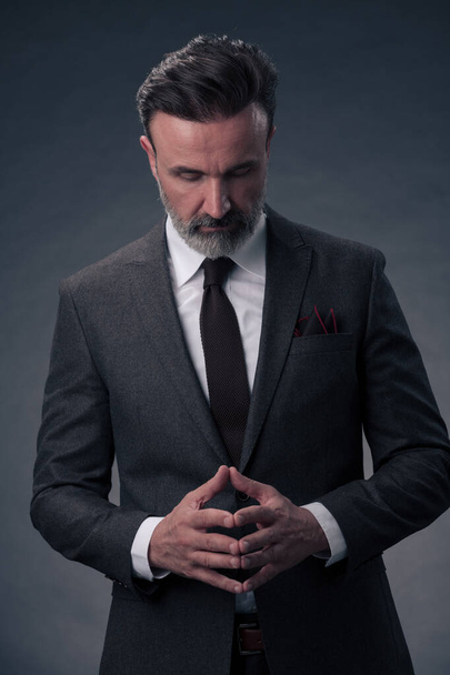 Portrait of a stylish elegant senior businessman with a beard and casual business clothes in photo studio isolated on dark background gesturing with hands. High quality photo - Φωτογραφία, εικόνα