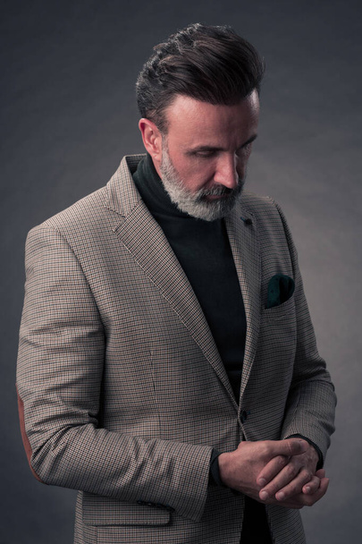 Portrait of a stylish elegant senior businessman with a beard and casual business clothes in photo studio isolated on dark background gesturing with hands. High quality photo - Foto, Imagem