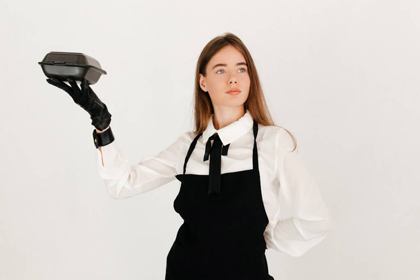 Молода офіціантка в білій сорочці і чорний фартух упаковує круасани, роблячи свою роботу в пандемічні часи
 - Фото, зображення