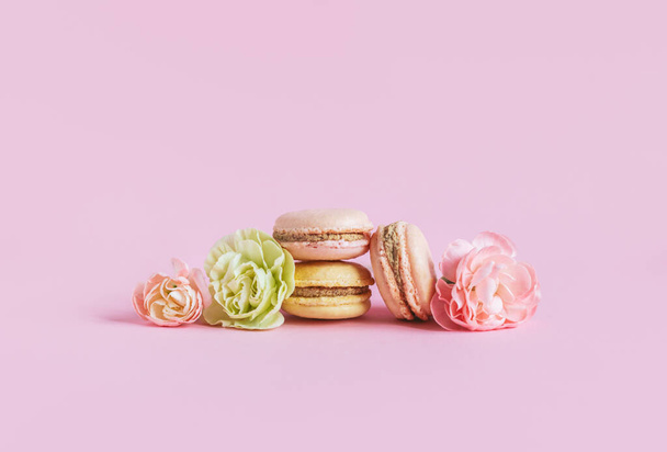 Chutné francouzské makaróny s květinami na růžovém pastelovém pozadí. Místo pro text. - Fotografie, Obrázek