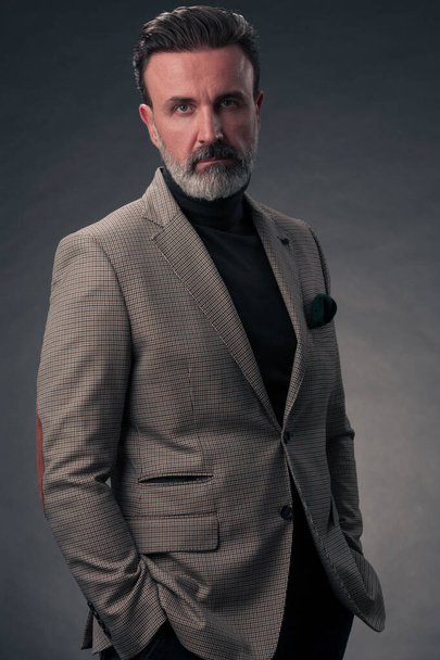 Portrait of a stylish elegant senior businessman with a beard and casual business clothes in photo studio isolated on dark background gesturing with hands. High quality photo - Fotoğraf, Görsel