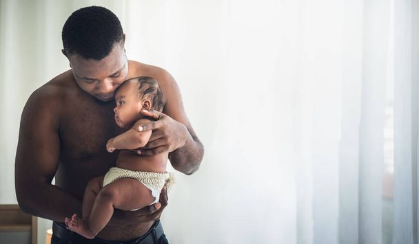 Padre africano sosteniendo a su hija, bebé recién nacido de 3 meses de edad, que es protección y feliz en un dormitorio blanco, concepto para la familia africana y el recién nacido - Foto, Imagen