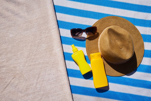 Жовта сонцезахисна кремова пляшка для захисту шкіри, сонцезахисні окуляри, солом'яний капелюх та пляжний рушник на синьому смугастому матраці. Концепція літнього відпочинку
 - Фото, зображення