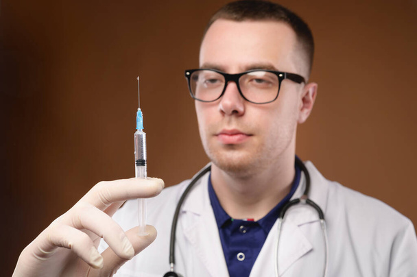 Young caucasian doctor man preparing to do a vaccination with a syringe. Studio shot on a brown background. Release air from the syringe before the injection - Photo, image