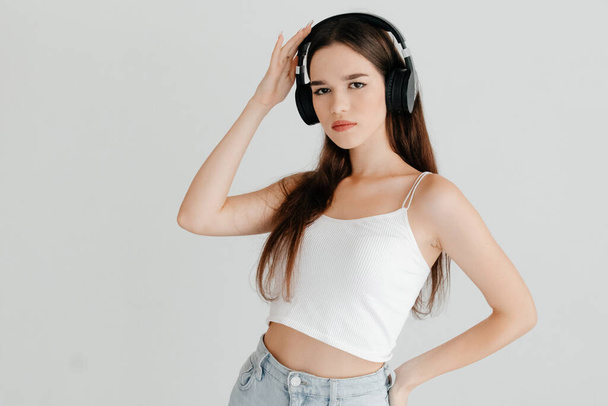 Young woman wearing casual clothes - white top and jeans, black headphones, listening to news. Worrying about today concept - Foto, Imagem