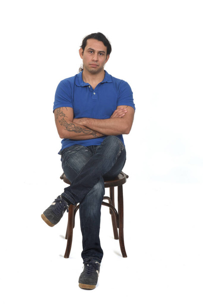 front view of man with ponytail and casual clothing legs and arms crossed sitting a chair on white background - Φωτογραφία, εικόνα