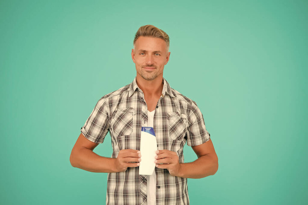 Guy hold bottle of mens hair shampoo blue background copy space, skincare - Photo, Image