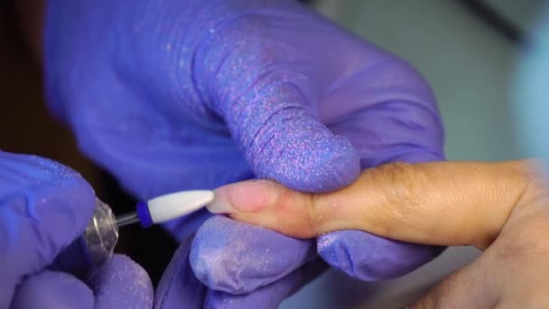 Manicure master in blue gloves removes gel polish from nails using a cutter. - Filmagem, Vídeo