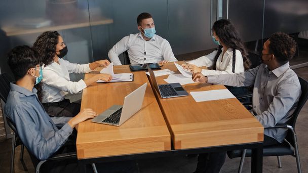 Багаторасові працівники в масці сидять в конференц-залі обговорюють колеги проекту активно сперечаються з менеджерами, які сидять в офісних бізнес-партнерах на зустрічі захисту від коронавірусної копії19
 - Фото, зображення
