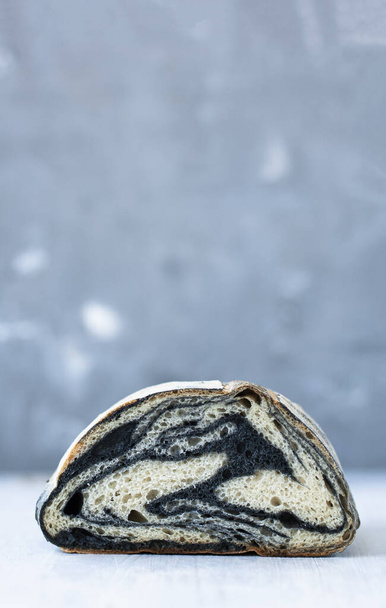 Ізольована половина домашнього хліба з каракатицьким чорнилом на сірому розмитому фоні
 - Фото, зображення