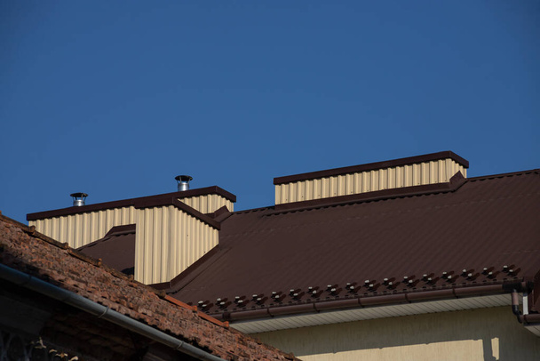 El techo de la casa está hecho de azulejos de metal rojo, una hermosa chimenea grande. - Foto, imagen