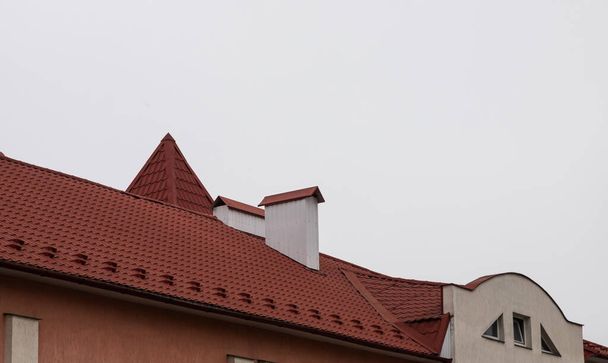 A ház teteje vörös fém csempékből készült, egy gyönyörű nagy kéményből.. - Fotó, kép