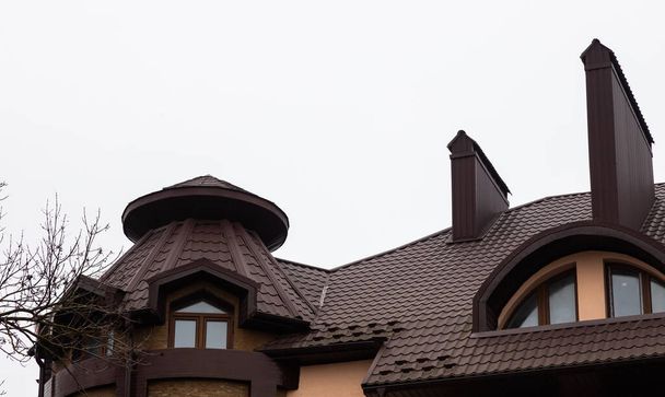 A ház teteje vörös fém csempékből készült, egy gyönyörű nagy kéményből.. - Fotó, kép