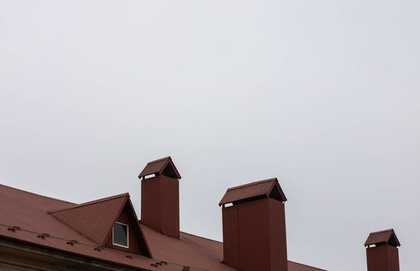 Η οροφή του σπιτιού είναι κατασκευασμένη από κόκκινα μεταλλικά πλακάκια, μια όμορφη μεγάλη καμινάδα. - Φωτογραφία, εικόνα